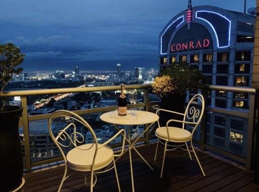 Night-time cityscape view from a balcony with a small table and two chairs