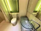 Modern bathroom with glass sink and illuminated green tile accent wall