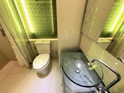 Modern bathroom with glass sink and illuminated green tile accent wall