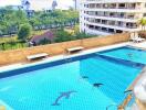 Outdoor swimming pool with dolphin tile design, lounge chairs, and city view