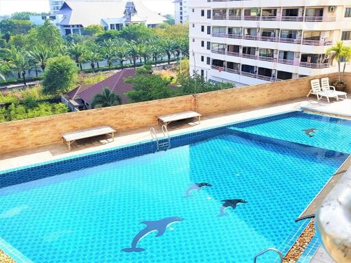 Outdoor swimming pool with dolphin tile design, lounge chairs, and city view