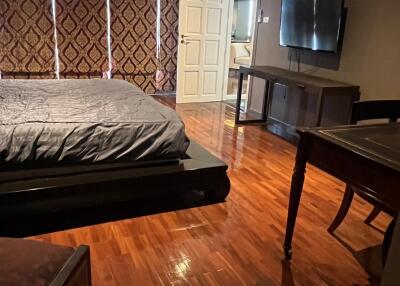 Spacious bedroom with hardwood floors, large bed, wall-mounted TV, and stylish drapes