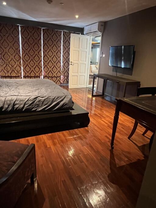 Spacious bedroom with hardwood floors, large bed, wall-mounted TV, and stylish drapes