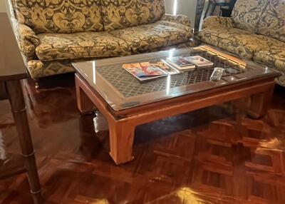 Living room with two patterned sofas, a glass-top wooden coffee table, and glossy parquet flooring