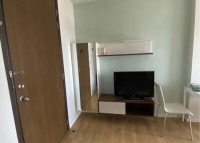 Living room with a TV, wooden floor, door, and a chair.