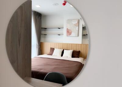 A well-lit bedroom with a large circular mirror, a cozy bed, and wall-mounted shelves