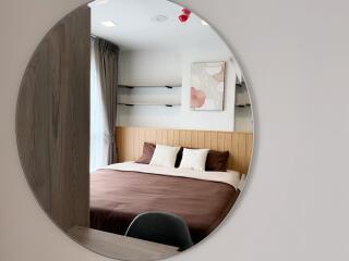 A well-lit bedroom with a large circular mirror, a cozy bed, and wall-mounted shelves