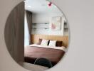 A well-lit bedroom with a large circular mirror, a cozy bed, and wall-mounted shelves