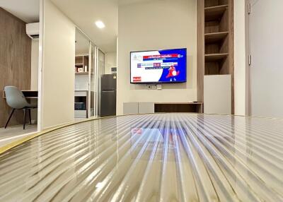 Modern living area with a wall-mounted TV and a view into the kitchen