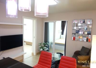 Modern living room with a mounted TV, red chairs, and a view into the bedroom