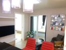 Modern living room with a mounted TV, red chairs, and a view into the bedroom