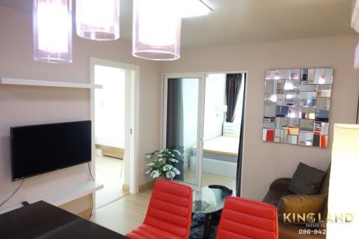 Modern living room with a mounted TV, red chairs, and a view into the bedroom