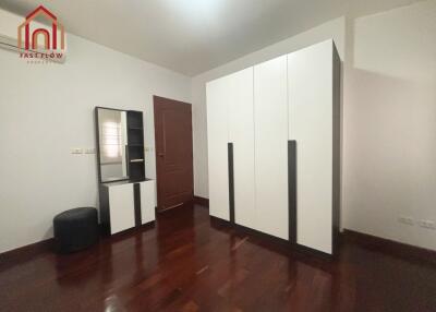 Modern minimalist bedroom with wooden floor, white wardrobe, small dresser, and upholstered stool