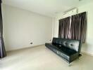 Minimalist living room with black leather couch and air conditioning.