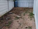 Unpaved backyard area with fencing and neighboring building