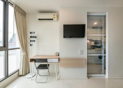 Living area with study desk, wall-mounted TV, air conditioning, and view of adjacent room