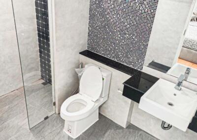 Modern bathroom with glass shower, toilet, and sink with black countertop.