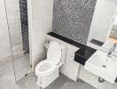 Modern bathroom with glass shower, toilet, and sink with black countertop.