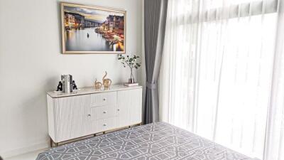 Bright bedroom with large window, white dresser, and decor