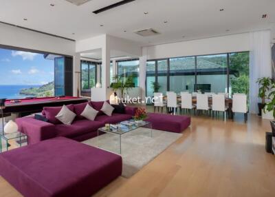 Modern living room with ocean view, large purple sectional sofa, pool table, dining area, and TV