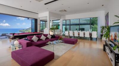 Modern living room with ocean view, large purple sectional sofa, pool table, dining area, and TV