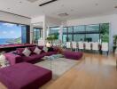 Modern living room with ocean view, large purple sectional sofa, pool table, dining area, and TV