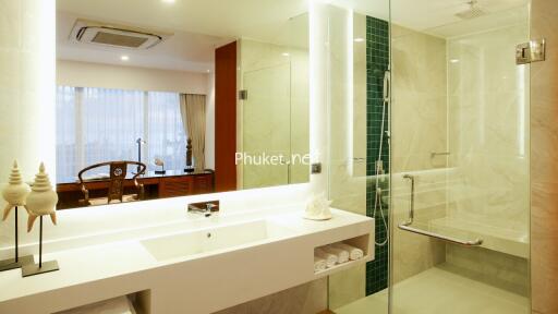 Modern bathroom with a large vanity mirror, white countertop, glass-enclosed shower, and decorative items