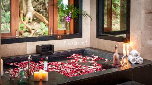 Luxurious bathroom with a large soaking tub filled with rose petals, candles, and a bottle of bath products.