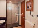 Modern bathroom with glass shower, wooden door, and wall-mounted sink