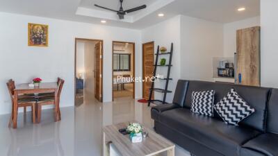 Modern living room with black sofa, decorative pillows, dining table, and ceiling fan