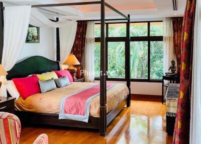 Spacious bedroom with a large four-poster bed, colorful bedding, and large windows offering a view of lush greenery.