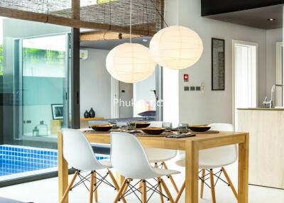 Modern dining area with wooden table and white chairs next to large windows overlooking a pool