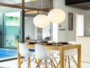 Modern dining area with wooden table and white chairs next to large windows overlooking a pool