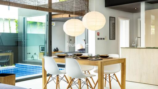 Modern dining area with wooden table and white chairs next to large windows overlooking a pool