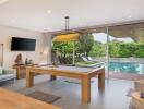 Modern living area with pool table and view of the outdoor pool and greenery