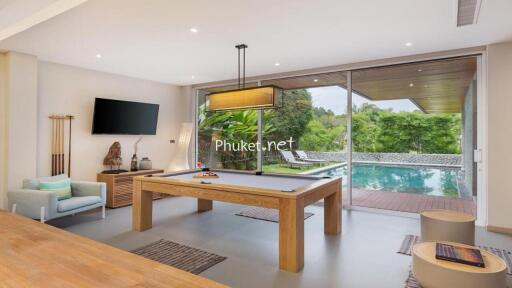 Modern living area with pool table and view of the outdoor pool and greenery