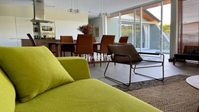 Modern living room with green couch, dining area, and large windows