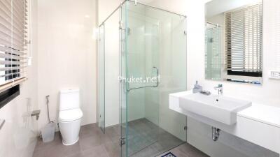 Modern bathroom with glass shower enclosure, wall-mounted sink, and toilet.