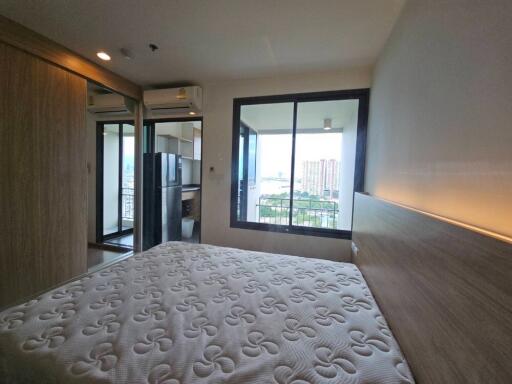 Modern bedroom with white mattress, wooden headboard, balcony view, and large sliding mirror door