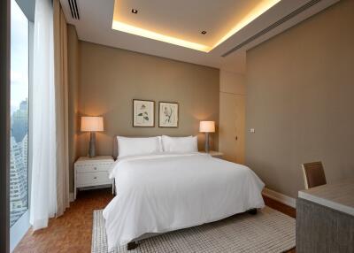 Modern bedroom with a large white bed, bedside tables and lamps, and large windows with city views