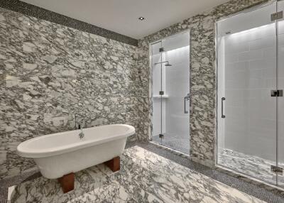 Luxurious bathroom with marble walls and floors, featuring a standalone bathtub and glass-enclosed showers