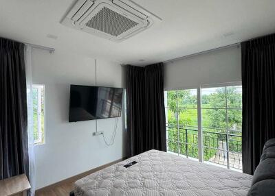 Modern bedroom with a large bed, wall-mounted TV, and balcony access.