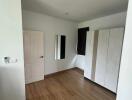 Bedroom with wooden floor, a door, a mirror on the wall, a window, and a wardrobe