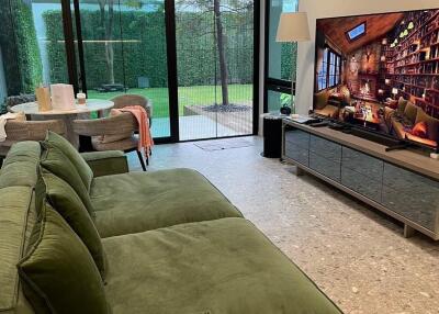 Modern living area with large green sofa, floor-to-ceiling windows, and a flat-screen TV.