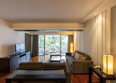 Spacious living room with large glass doors leading to a balcony with outdoor seating and greenery beyond