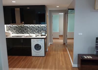 Modern kitchen with wooden flooring, black cabinets, tiled backsplash, and a washing machine