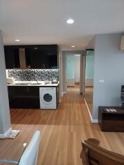 Modern kitchen with wooden flooring, black cabinets, tiled backsplash, and a washing machine