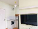 Compact kitchen area with white cabinetry and mounted TV