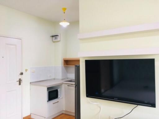 Compact kitchen area with white cabinetry and mounted TV