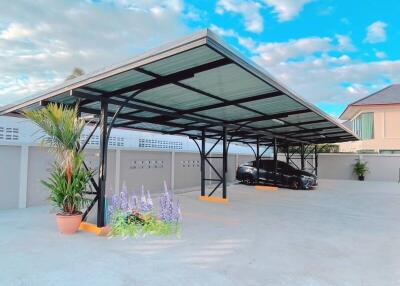 Carport area with a black car parked under a metal roof next to potted plants and flowers